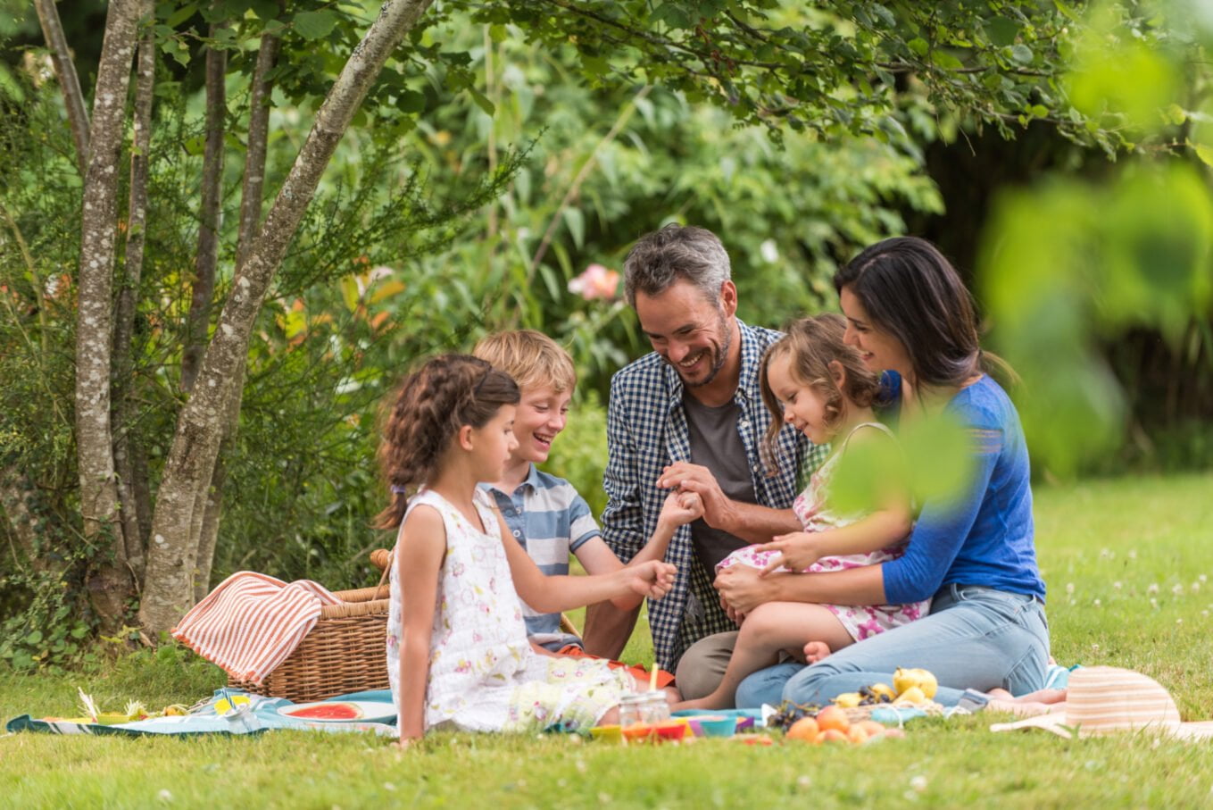 Cheerful,Family,Sitting,On,The,Grass,During,A,Picnic,In